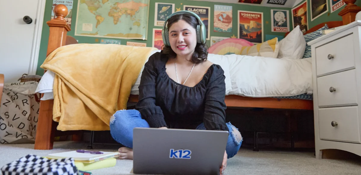 Student attending to an online class in her rooms wearing a light green pair of headphones